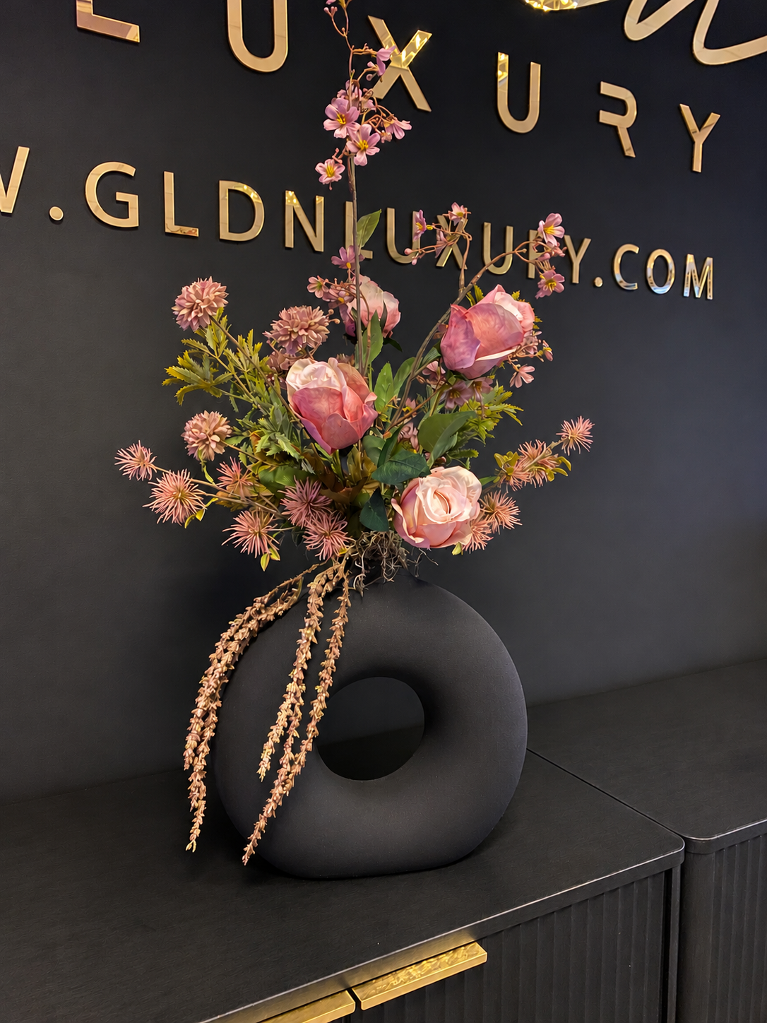 Luxe oudroze kunstbloemstuk met roze rozen, naturelaccenten en organische zwarte designvaas van GLDN Luxury.