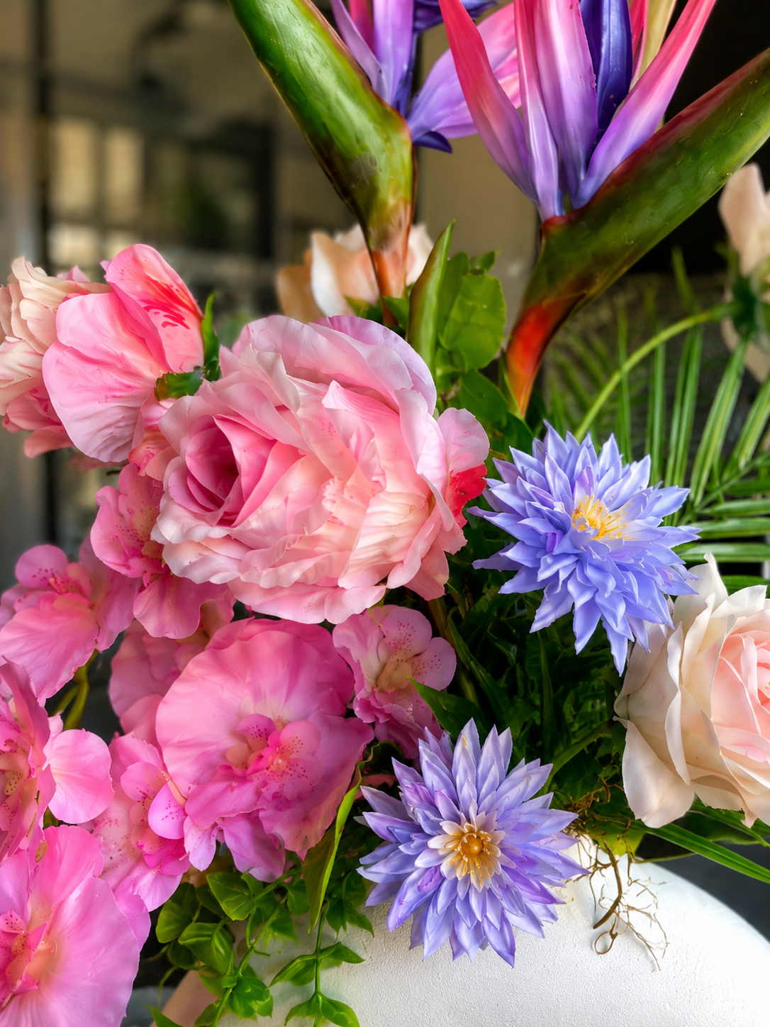Bouquet de fleurs artificielles rose et violet avec des oiseaux de paradis dans un vase blanc
