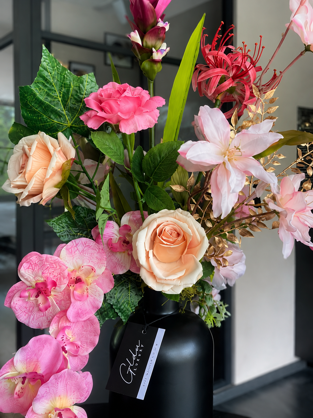 Luxe roze kunstbloemstuk met orchideeën, rozen, exotische bloemen en gouden accenten in een zwarte design vaas, ruim 70 cm hoog.